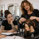 Beauty instructor demonstrating hair sectioning to adult students in a cosmetology training classroom.